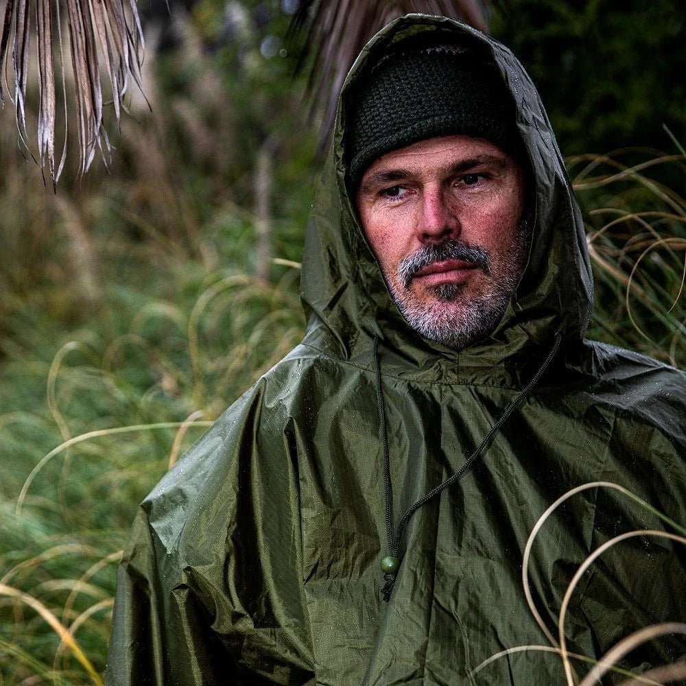 Arcturus waterproof green rain poncho for hiking, camping, and emergency survival, shown worn outdoors in wet weather
