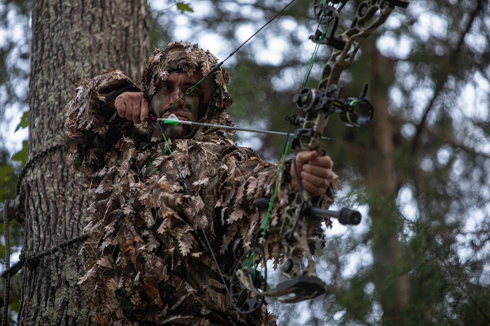 Person wearing Arcturus Realtree EDGE 3D Leafy Ghillie Suit shooting a bow in a tree stand